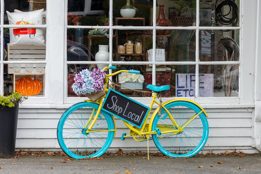 A colorful bicycle with flowers and 'Shop Local' sign outside a store in Sudbury, MA.