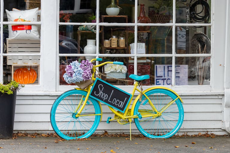 A colorful bicycle with flowers and 'Shop Local' sign outside a store in Sudbury, MA.
